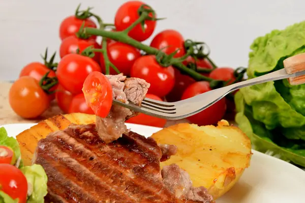 フォークに焼き肉トマトとオリーブをホワイトプレートに乗せたレタスの隣に焼いたジャガイモ — ストック写真