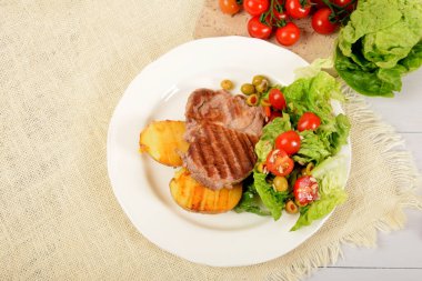 İki parça kızarmış patates ve yanında da salata, domates ve beyaz bir tabakta zeytin.