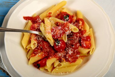 Makarna üzerine domates sosu ve rendelenmiş peynir serpilmiş küçük domatesler.