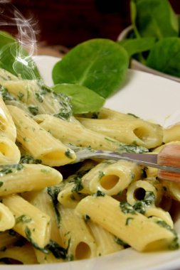 Beyaz tabakta ıspanak soslu makarna yanında taze ıspanak yaprakları ve ahşap mutfak tahtasındaki mavi peynir.