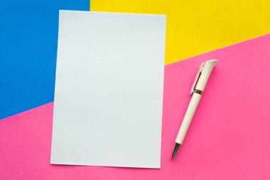 Geometrik pembe, sarı ve mavi arka planda beyaz model ve kalem. Düz konum, üst görünüm, kopyalama alanı