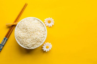 Bir kasede kuru beyaz pirinç ve parlak sarı arka planda Çin yemek çubukları. Düz konum, üst görünüm, kopyalama alanı