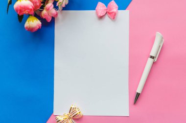 Mavi ve pembe arkaplanlı bir kalem ve bir buket çiçekle düz bir fotoğraf. Sevgililer Günü ya da Anneler Günü tebrik kartı