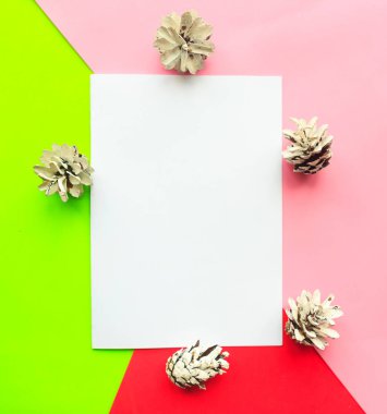 Geometrik pembe, yeşil ve kırmızı arka planda kozalaklı beyaz Noel kartı dekorasyonu. Düz konum, üst görünüm, kopyalama alanı