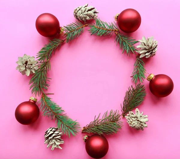 Christmas wreath of spruce branches, red baubles and pinecones on pink background. Flat lay, top view, copy space