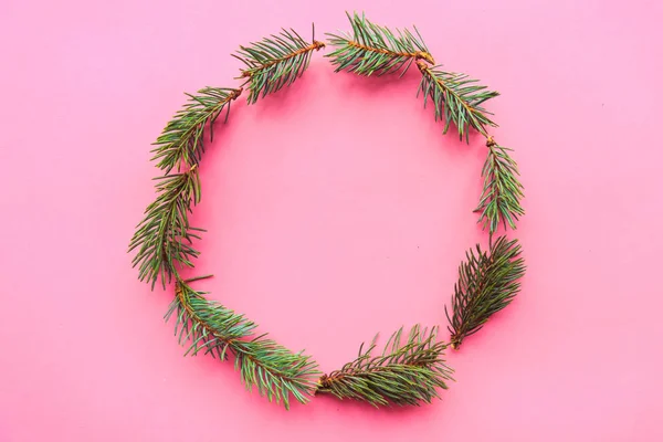 Christmas wreath of spruce branches on pink background. Flat lay, top view, copy space