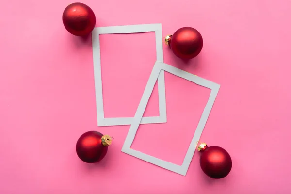 Merry Christmas and Happy New Year. Flat lay photo with white mockup photo frames and red balls on pink background. Minimal concept. Xmas greeting card, banner. Copy space for the text