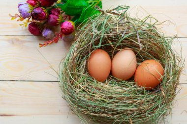 Samanlıkta üç çiğ yumurta ve ahşap masada bir buket çiçek. Paskalya konsepti