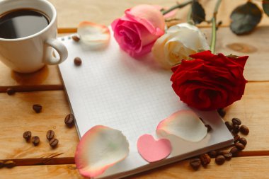 Kahve fincanı, gül buketi ve ahşap arka planda not defteri.