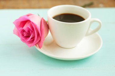 Kahve fincanı ve ahşap masada pembe gül.