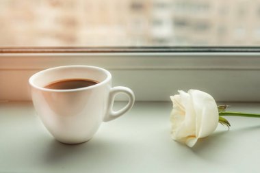 Kahve fincanı ve pencere eşiğinde beyaz gül.