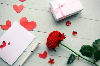 Love composition - red rose, gift box and greeting card on wooden background, top view. Wedding or Valentine concept