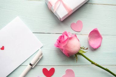 Love composition - pink rose, gift box and greeting card on wooden background, top view. Wedding or Valentine concept