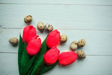 Red craft tulips and quail eggs on wooden background, top view. Easter concept
