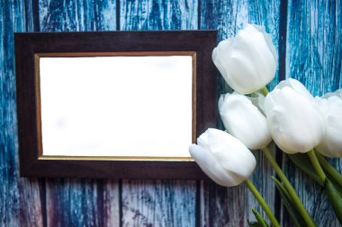 Beyaz lale buketi ve ahşap arka plandaki fotoğraf çerçevesi.