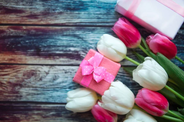 Bouquet of red and white tulips and gift boxes on wooden background, top view. Copy space for the text