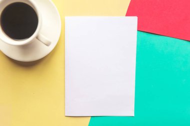 Beyaz model boş ve kahve fincanı geometrik sarı, kırmızı ve yeşil arka planda. Ofis kavramı