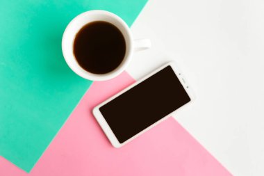 Geometrik pembe, beyaz ve yeşil kağıt arka plan dokusu üzerine model telefon ve kahve fincanı