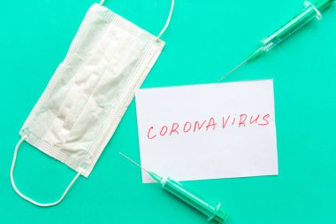 Yeşil arka planda tıbbi maske ve tek kullanımlık şırıngalar. Çin Coronavirüs Hastalığı covid-19