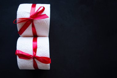 Siyah arka planda hediye yayı ile sarılmış tuvalet kağıdı ruloları. Covid19 konsepti