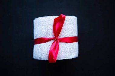 Siyah arka planda hediye yayı ile sarılmış tuvalet kağıdı rulosu. Covid19 konsepti