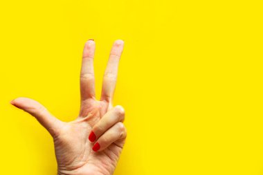 Kadının eli parlak sarı arka planda zafer jestini gösteriyor. Minimum konsept. Metin için alanı kopyala