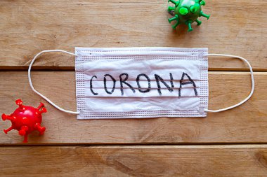 Corona sözcüğüyle tıbbi maske ve tahta arka planda virüs modelleri. Covid-19 konsepti