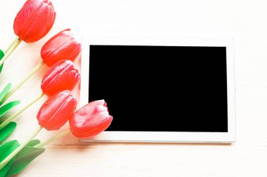 Ahşap zemin üzerinde kırmızı laleler ve siyah model tablet. Anneler Günü tebrik kartı.