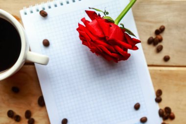 Model defterini aç, kahve fincanı ve tahta arka planda kırmızı gül. Güzel tebrik kartı.