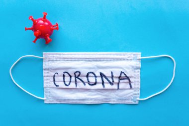 Mavi arka planda Corona ve kırmızı koronavirüs modelli tıbbi maske. Minimum konsept. Covid-19 konsepti