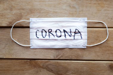 Tahta arka planda Corona sözcüğüyle tıbbi maske. Covid-19 konsepti
