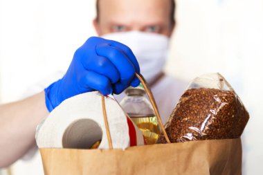 Koruyucu maskeli ve tıbbi eldivenli teslimatçı paket yemek getiriyor. Karantina döneminde yiyecek teslimatı. Covid-19 konsepti