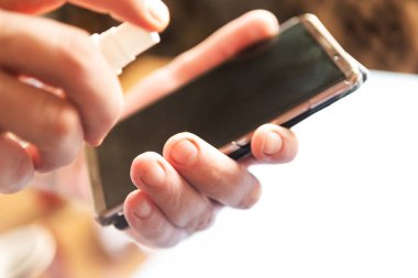 Adam telefonu el dezenfektanı ile siler. Covid 19 konsepti.