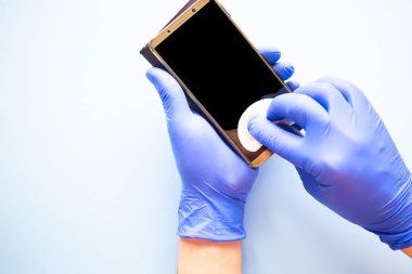 Eldivenli adam telefonu pamuklu süngerle siler. Covid 19 konsepti