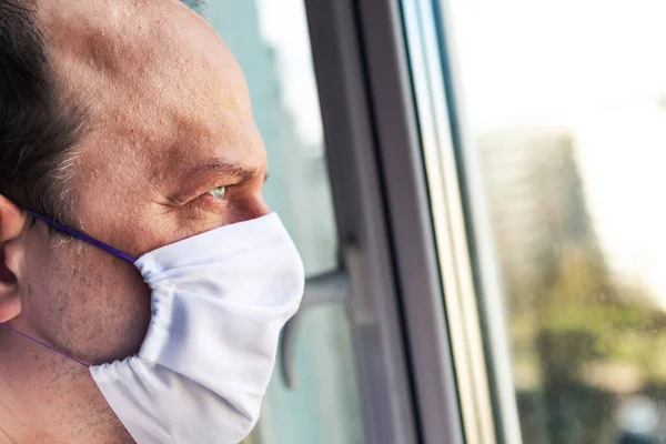 医療保護マスクの男が窓の外を見ている コロナウイルスの概念 検疫の概念 — ストック写真