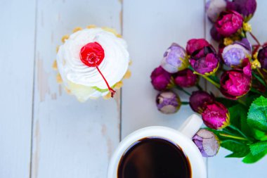 Düz bir fotoğraf, taze pasta, bir buket çiçek ve ahşap arka planda kahve fincanı.