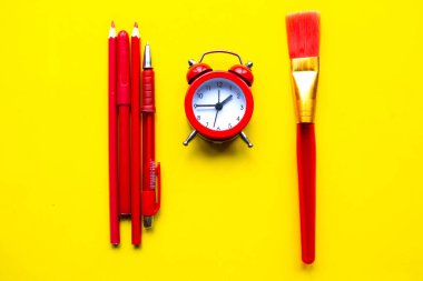 Kalemler, çalar saat ve parlak sarı arka planda boya fırçası. Okul konseptine geri dönelim. Asgari konsept