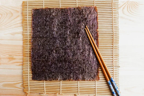 Chinese chopsticks and sushi mat with seaweed background. Copy space for the text
