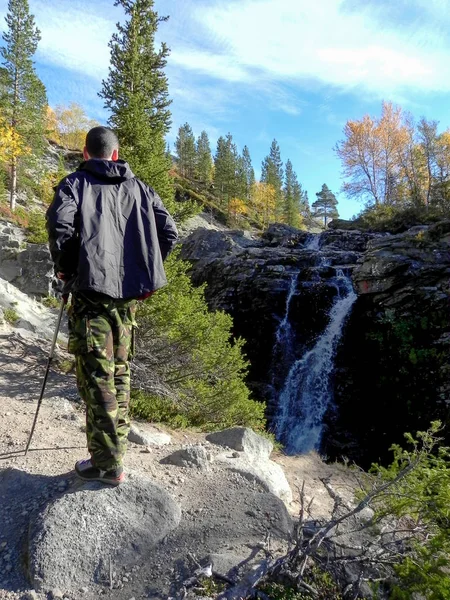 A man in a black jacket from the back against the backdrop of a waterfall in the fall