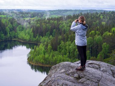 Kadın dürbünden bakar. bir göl yakınındaki bir ormanda bir kaya üzerinde turist kız
