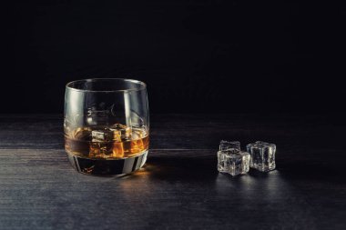 Viski bardağa sıçrıyor, tahta masanın üstünde buz var.