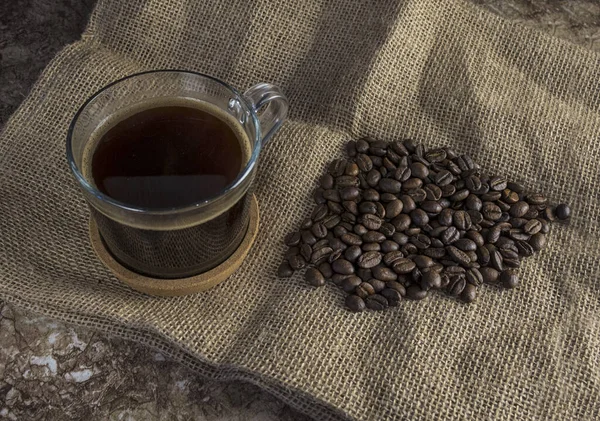 Dark roasted coffee beans on burlap and a mug of freshly brewed natural coffee — Stock Photo, Image