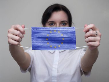Bir kadın elinde Avrupa Birliği bayrağının görüntüsüyle tıbbi bir maske tutuyor. Coronavirus COVID-19