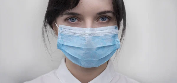 Portrait of a young European woman in a protective disposable medical mask. Concept of caronavirus Cavid 19 and human quarantine. Girl in a mask on a white wall. Masked medical worker