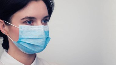 Korunabilir tıbbi maske takan genç Avrupalı bir kadının portresi. Caronavirus Cavid 19 ve insan karantinası kavramı. Beyaz duvarda maskeli bir kız. Maskeli sağlık görevlisi.