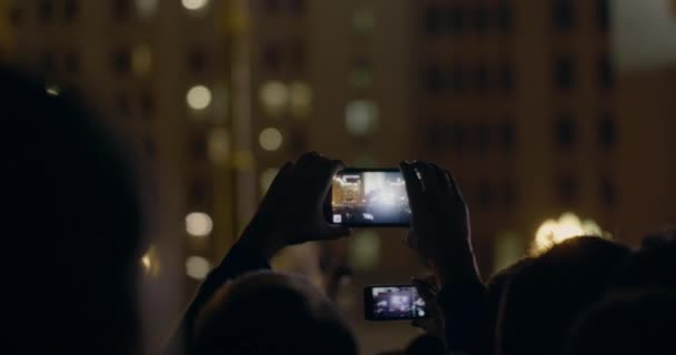 Widok z tyłu ręce trzymać smartfonu wśród ludzi rave party z światła — Wideo stockowe