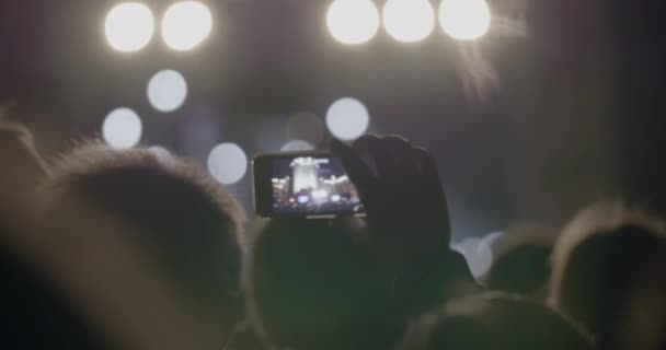 Vista desde detrás de las manos mantenga el teléfono inteligente entre las personas en la fiesta rave con luz — Vídeo de stock