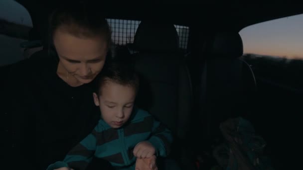 Vue de la femme avec son fils dans l'obscurité équitation en voiture sur le siège arrière, regarder la tablette d'ordinateur — Video