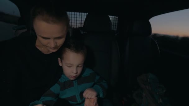 View of woman with son in the dark riding in car on back seat, watching computer tablet — Αρχείο Βίντεο