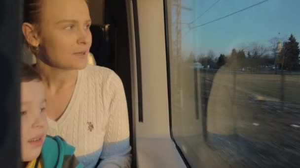 そのレールの鉄道場所の窓に座って、外を見て母と小さな男の子 — ストック動画